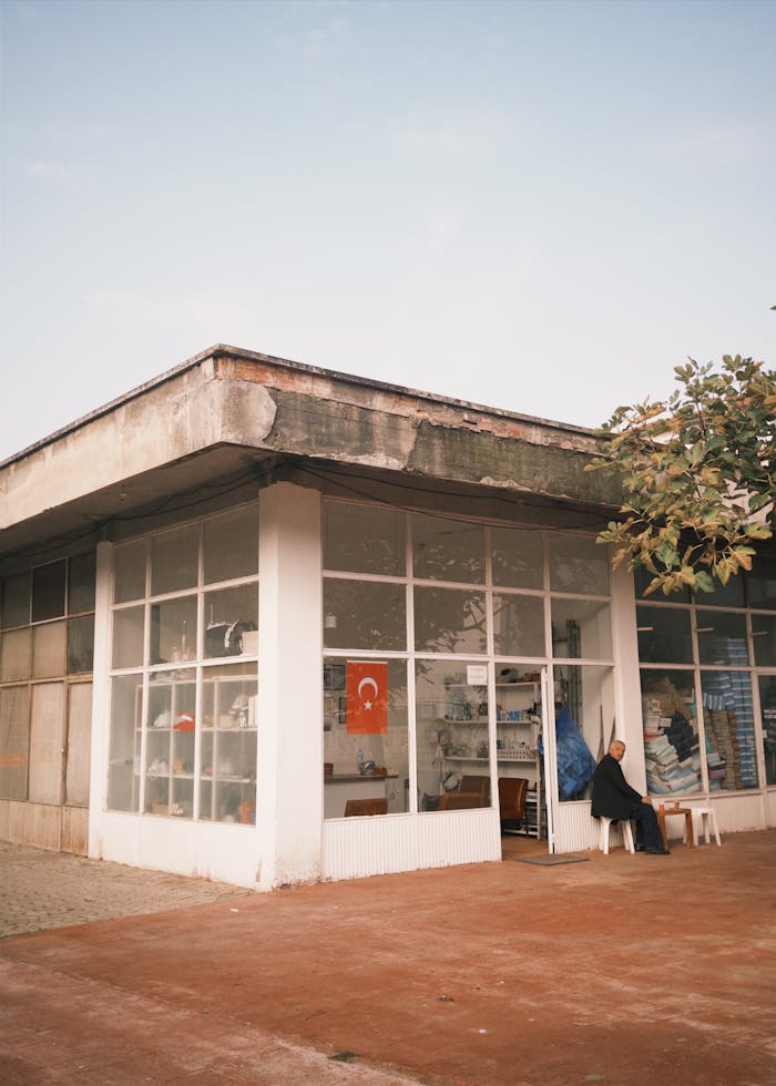Street view of a shop with Turkish flag and a person sitting outside under clear sky.